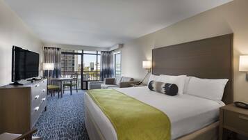 A hotel room with a large bed, a desk with a chair, a television, and a view of the city through large windows.