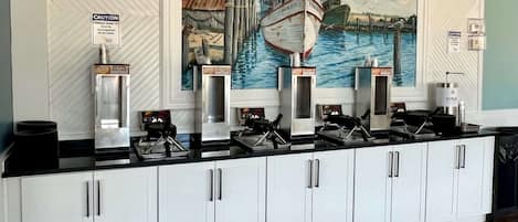 A kitchen with a mural of boats on the wall, a coffee station, and a self-serve beverage dispenser.