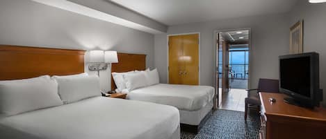 Habitación de hotel con dos camas, televisión, lámpara y vistas al balcón.