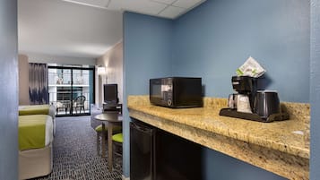 Habitación de hotel compacta con kitchenette, microondas, cafetera y refrigerador. Incluye una pequeña mesa de comedor y una silla, además de vistas al balcón exterior.
