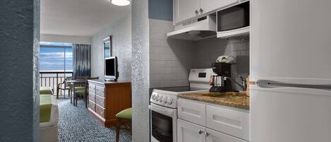 A modern kitchen with white cabinets, a microwave, and a stove. There is a dining area with a table and chairs, and a view of the sky through a window.