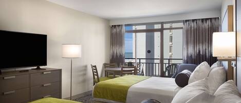 A hotel room with two beds, a TV, a desk, and a balcony with curtains.