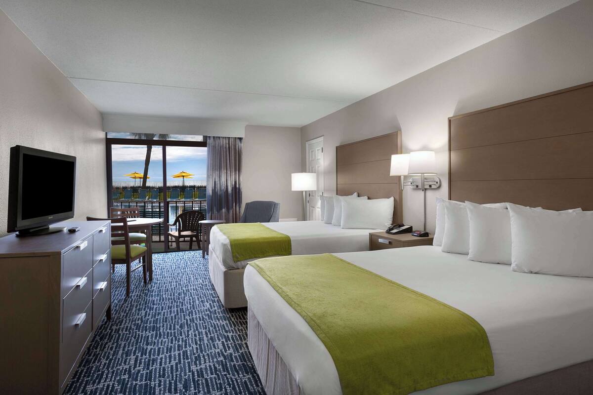 Une chambre d’hôtel avec deux lits, une télévision, un bureau avec une chaise, une lampe et une vue sur la piscine.