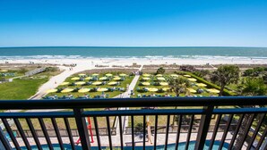 Vista da praia a partir de uma varanda, com piscina, guarda-sóis e espreguiçadeiras.