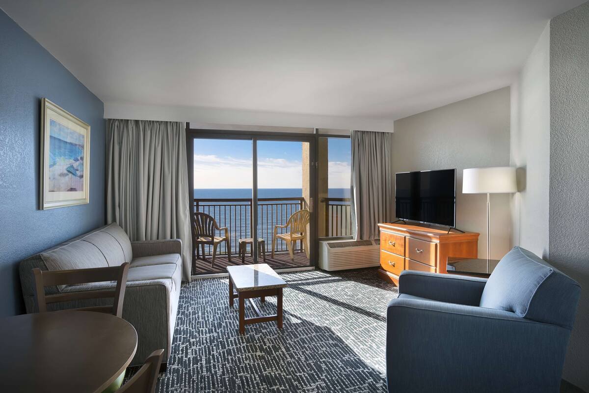 Une chambre d’hôtel avec un balcon, un canapé, une table, une télévision et une commode.