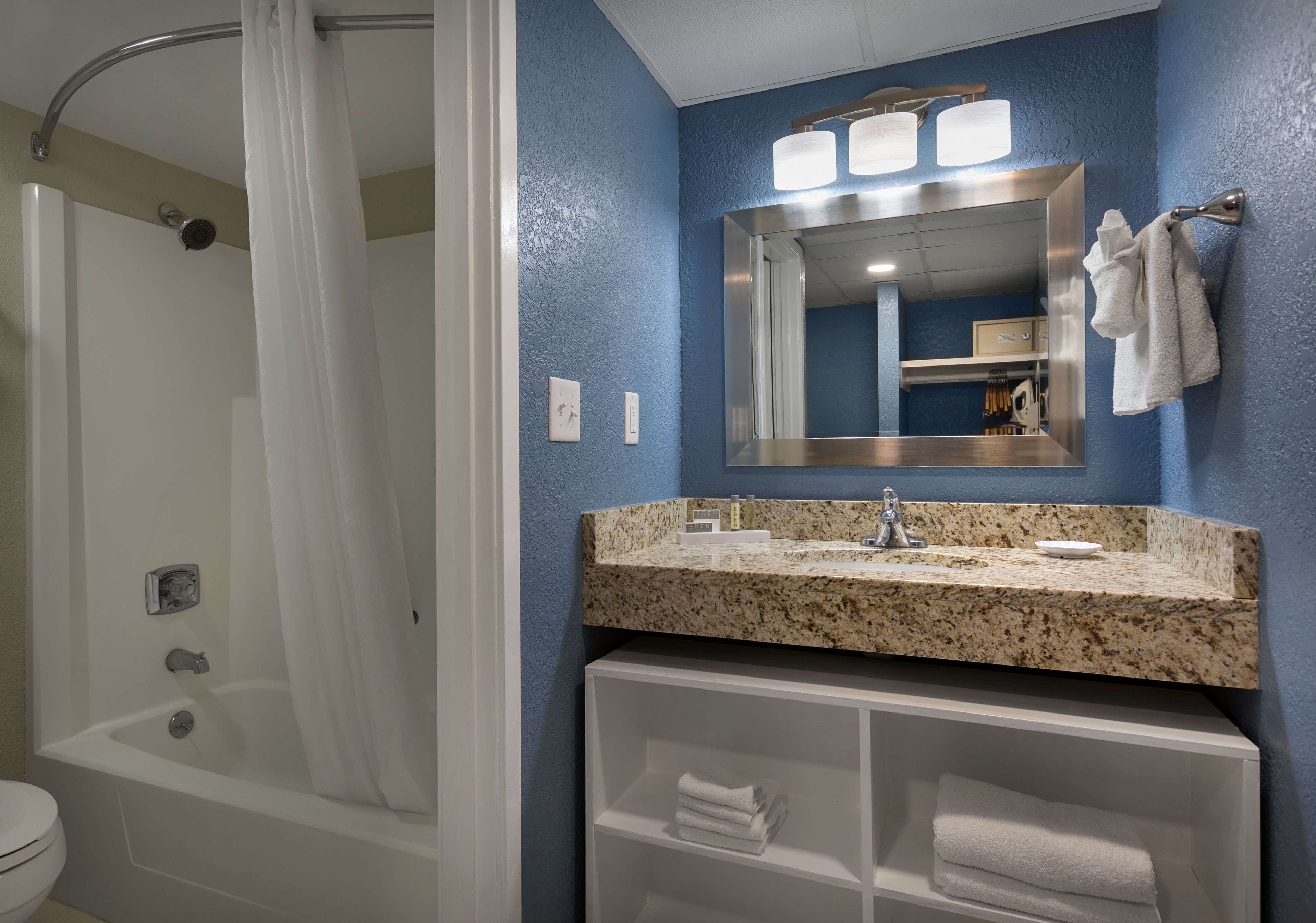 Une salle de bain avec une douche, un lavabo doté d’un plan de travail en granit, un miroir et un porte-serviettes.