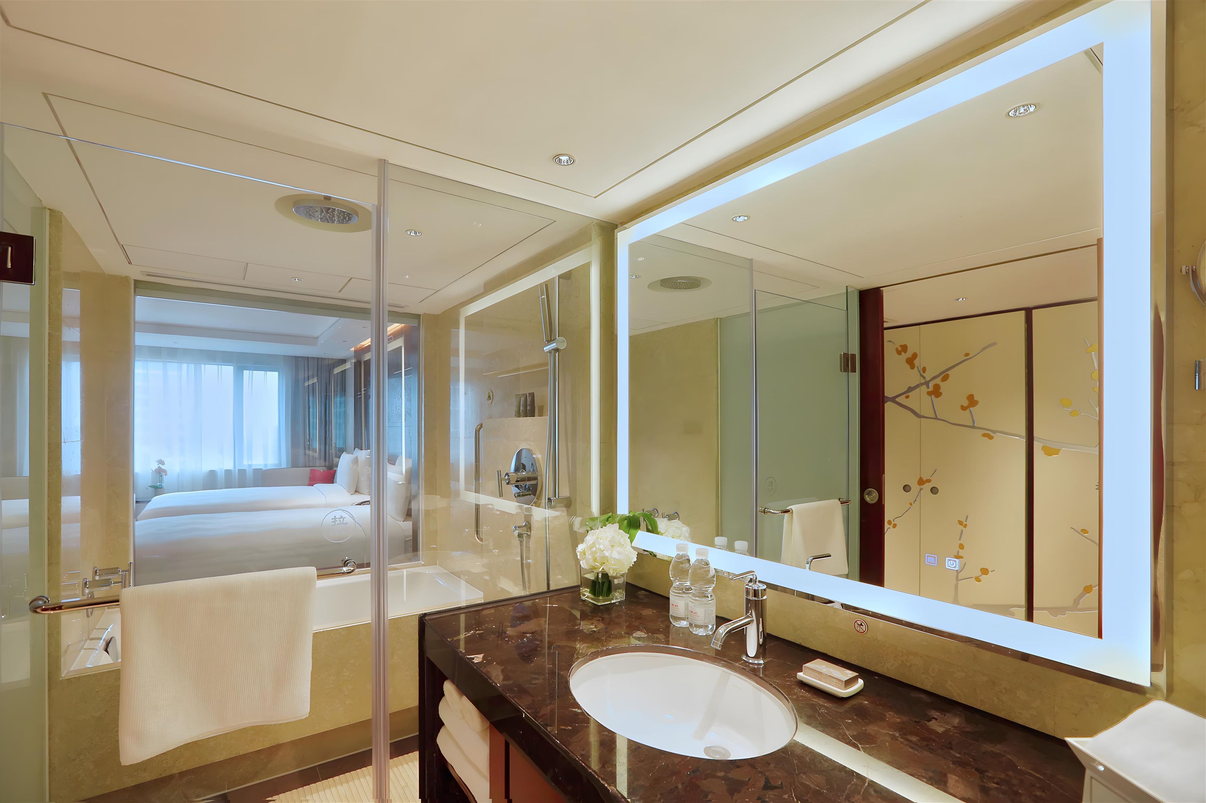 A modern hotel bathroom with a large mirror, a sink, and a glass shower enclosure.