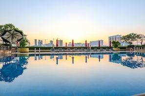 A swimming pool with lounge chairs and umbrellas, surrounded by greenery and high-rise buildings in the background. - China Hotel, Guangzhou (Guangzhou)