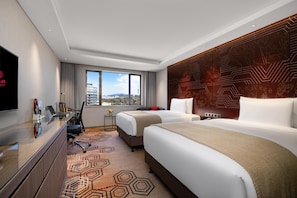 Habitación de hotel con dos camas, un escritorio, un televisor y vista a la ciudad.