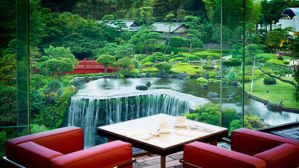 A view of a waterfall through a glass window, with red seating and a table in the foreground.