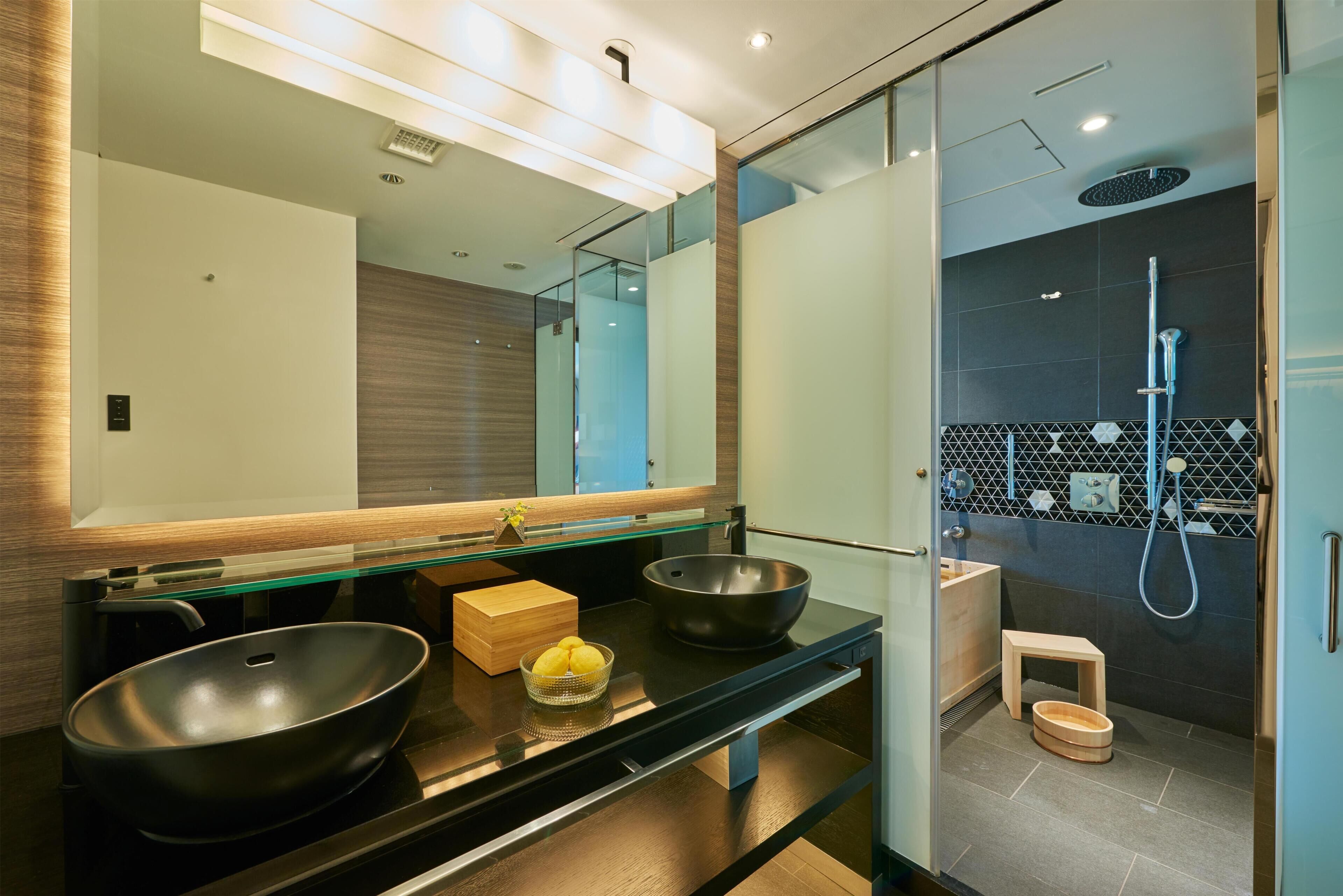 Un bany modern amb una cabina de dutxa de vidre, un mirall gran i un lavabo negre amb forma de bol.