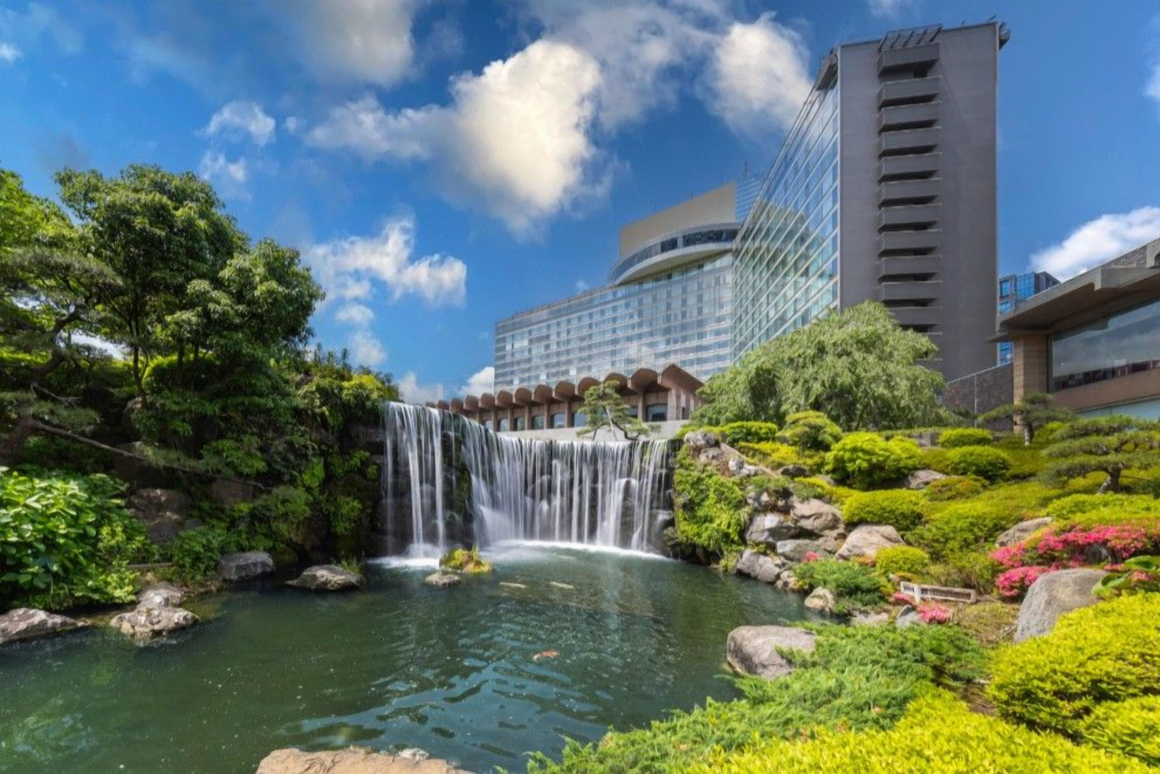 A waterfall in a landscaped area with a modern building in the background.