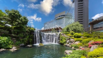 A waterfall in a landscaped area with a modern building in the background.