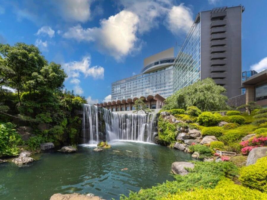 Uma cascata em área ajardinada com um edifício moderno ao fundo.
