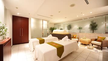 Two single beds with white linens and green throw pillows, a comfortable sofa, and a wooden wardrobe offer a cozy retreat.