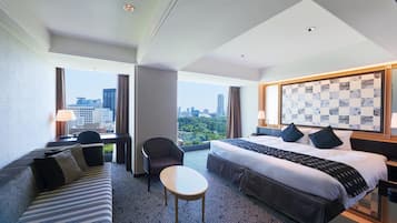 Ein Hotelzimmer mit einem großen Bett, einer Couch, einem kleinen Tisch und Blick auf die Stadt.