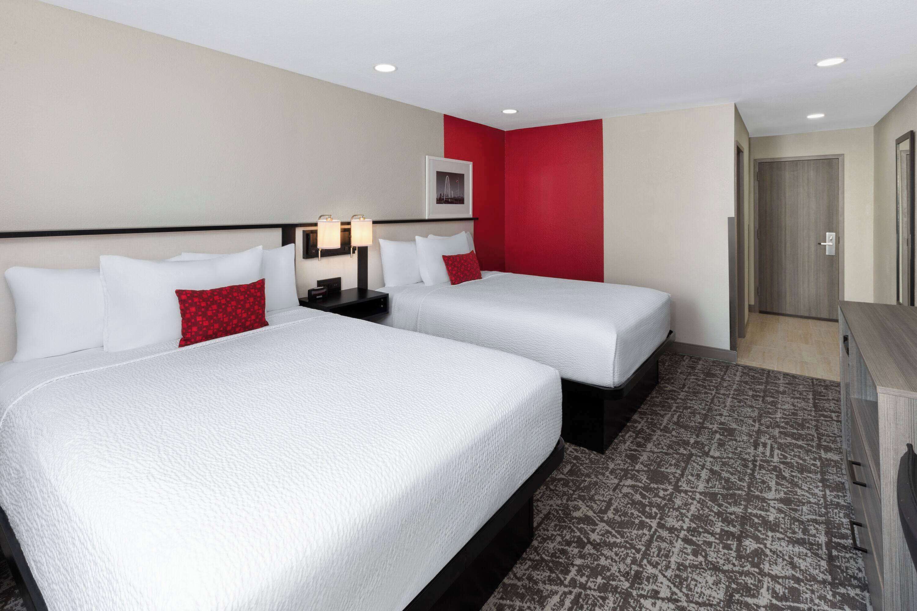 Une chambre d’hôtel avec deux lits, un mur d’accent de couleur rouge et une moquette à motifs.