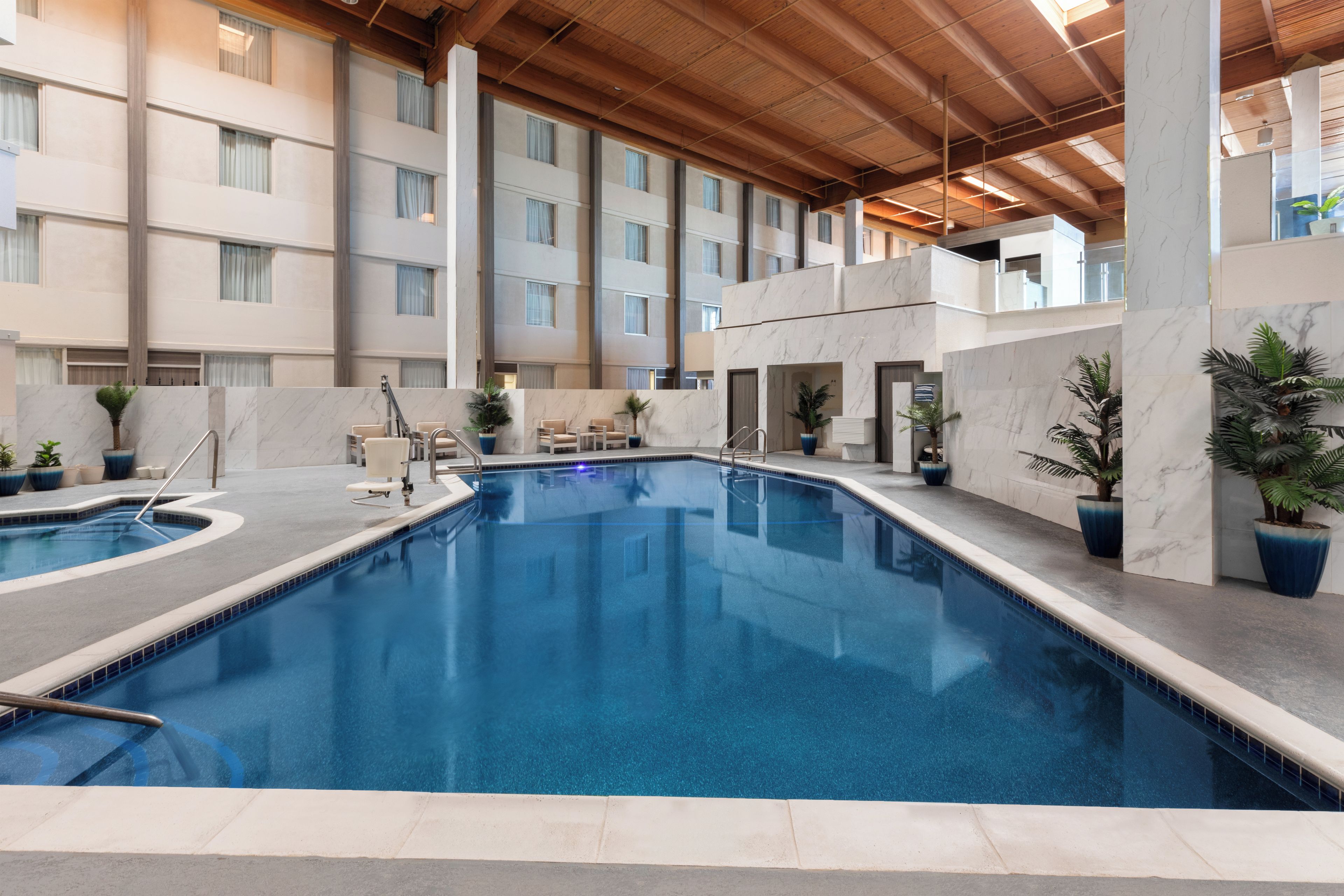 An indoor swimming pool with a clear blue water surface, surrounded by marble walls and potted plants.