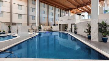An indoor swimming pool with a clear blue water surface, surrounded by marble walls and potted plants.