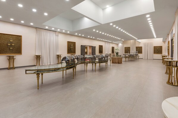 Un hall d’hôtel spacieux, doté d’une longue table en verre, d’élégants éléments décoratifs dorés et d’un éclairage moderne.
