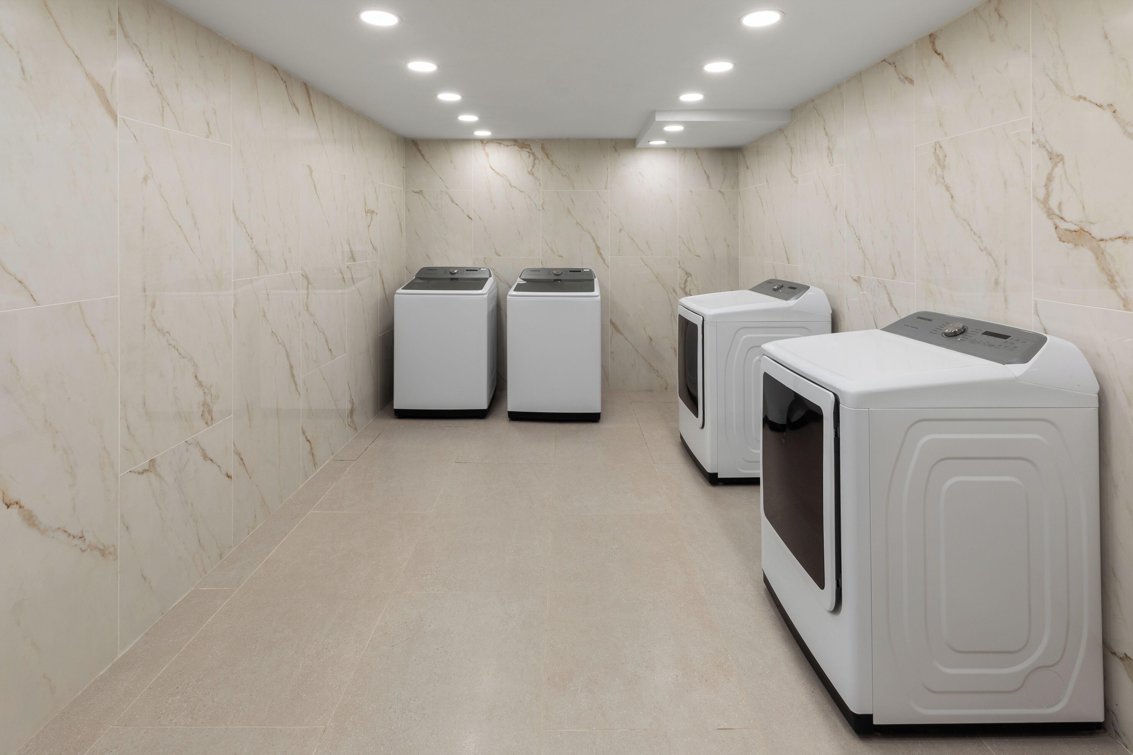 A laundry room with three washing machines and a dryer, marble walls, and a tiled floor.