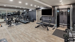A modern gym with various exercise equipment, a large mirror, and a TV screen.