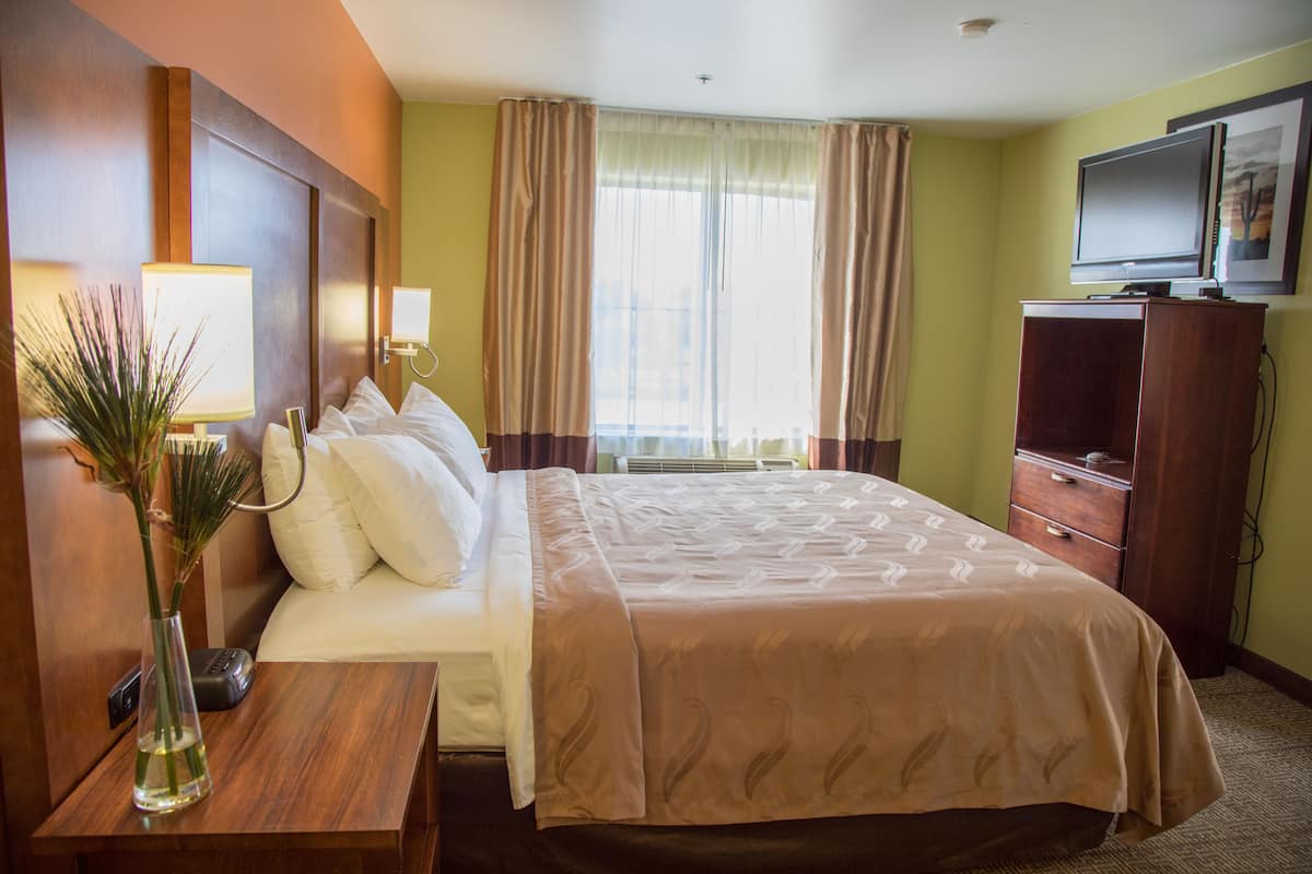 A hotel room with a bed, bedside lamps, a TV, a dresser, and a window with curtains.
