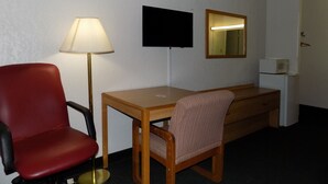 A hotel room with a wooden desk, a red chair, a lamp, a flat-screen TV, a mirror, and a microwave. - Topeka Plaza Inn (Topeka)