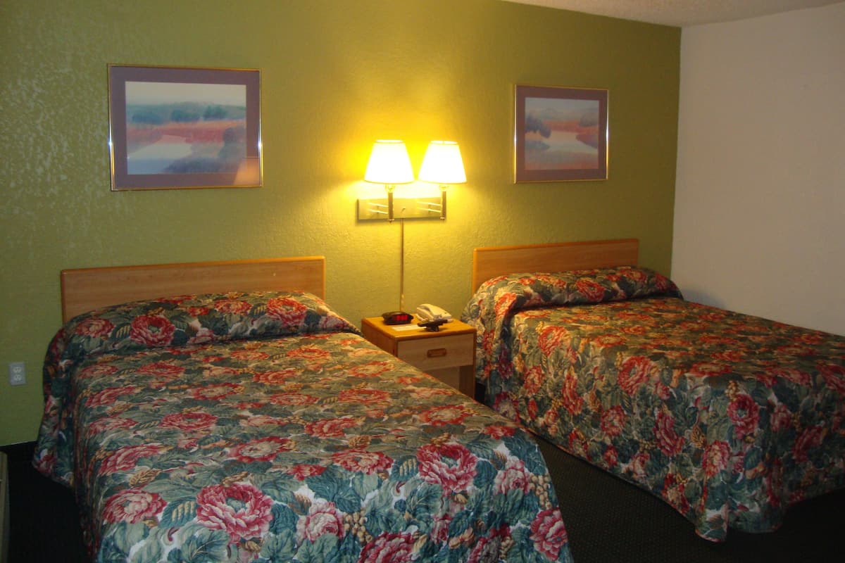 A hotel room with two beds, each with floral bedding, a nightstand with a lamp, and two framed pictures on the wall.