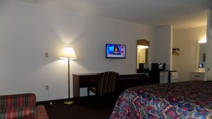 A hotel room with a bed, a desk, a chair, a TV, and a lamp. - Topeka Plaza Inn (Topeka)