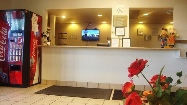 A reception area with a Coca-Cola vending machine, a television screen, and a wooden table with a vase of roses. - Topeka Plaza Inn (Topeka)