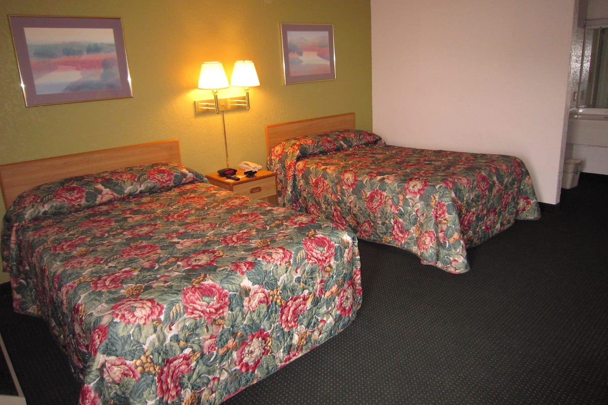 A hotel room with two beds, each with floral bedding, a nightstand with a lamp, and two framed pictures on the wall.