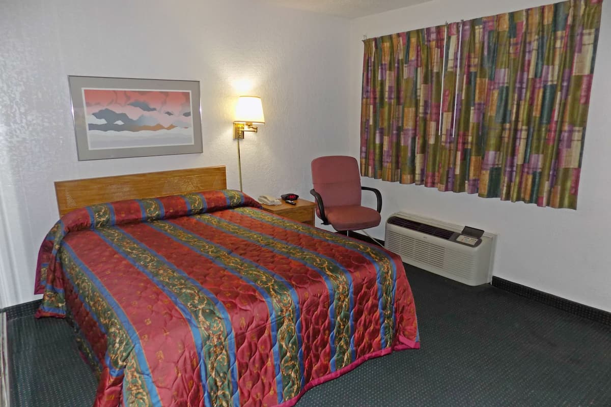 A hotel room with a bed, a chair, a lamp, a heater, and a curtain.