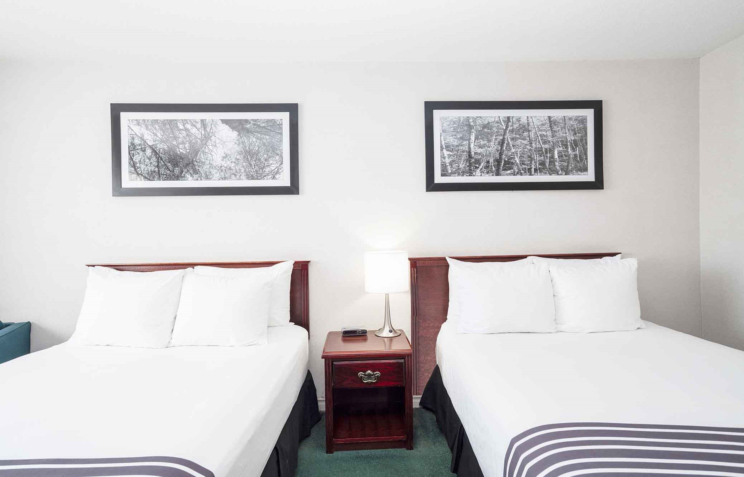 Habitació d'hotel amb dos llits individuals, una tauleta de nit amb una làmpada i dos quadres al mur.