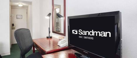 Habitación de hotel con una televisión que muestra el logo de Sandman Inn, un escritorio con una lámpara, una silla y un teléfono.