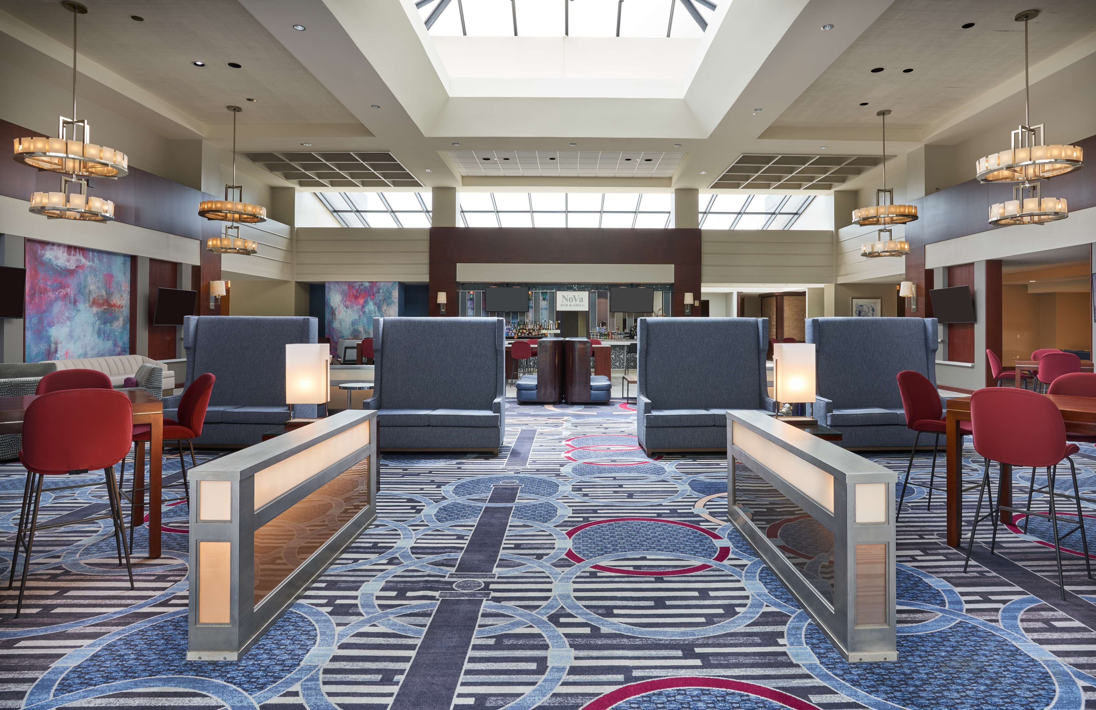 Un vestíbulo de hotel con techo alto, candelabros modernos, alfombra estampada y un mostrador de recepción.