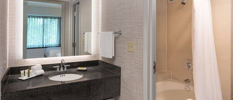 A modern bathroom with a granite countertop sink, a large mirror, and a shower with a white curtain.