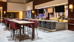 A modern bar area with a counter, seating, and a large screen. - Hilton Fairfax (Fairfax)