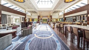 A spacious lobby with a high ceiling, a central bar area, and seating arrangements. - Hilton Fairfax (Fairfax)