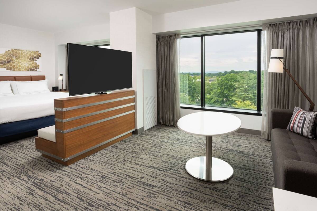 A hotel room with a bed, a TV, a desk, a sofa, and a large window with a view.