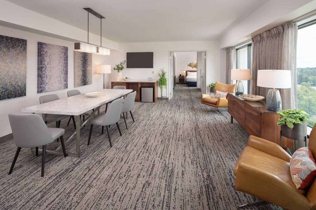 A modern hotel room with a dining area, a sofa, and a view of the outdoors.