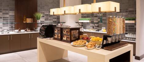 A modern kitchen with a buffet setup, featuring a central island with food items, a coffee machine, and a variety of containers for beverages.