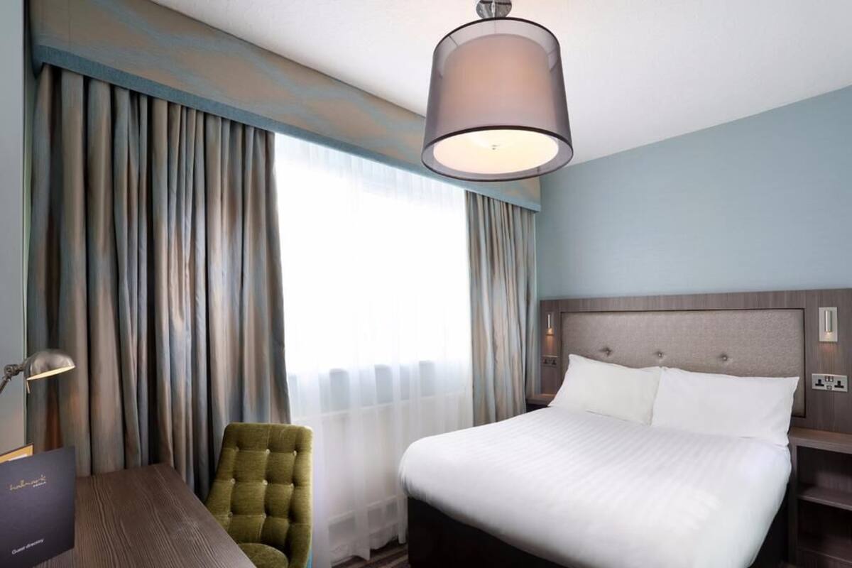 A hotel room with a bed, a desk, a chair, and a large window with curtains.