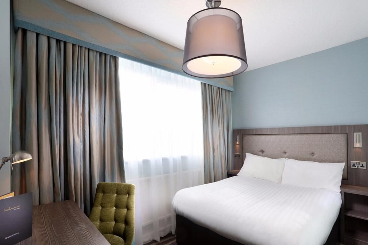 A hotel room with a bed, a desk, a chair, and a large window with curtains.