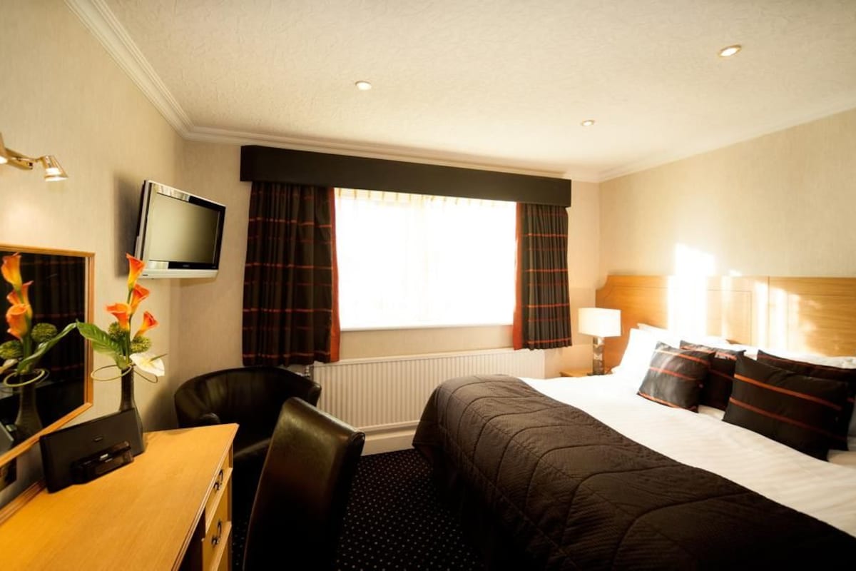 A hotel room with a bed, a desk with a computer, a chair, a television, and a window with curtains.