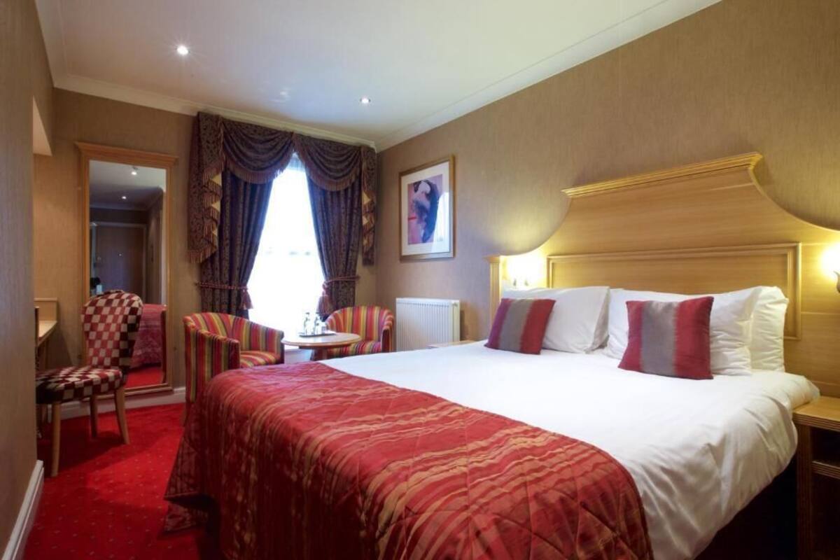 A hotel room with a large bed, a desk, a chair, and a window with curtains.