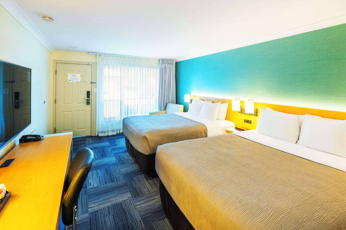 A hotel room with two beds, a desk, a chair, and a television.