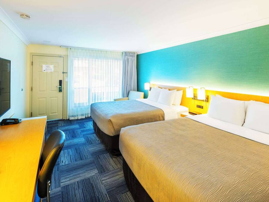 Une chambre d’hôtel avec deux lits, un bureau, une chaise et un téléviseur.