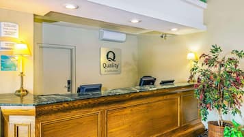 A hotel reception area with a wooden reception desk, a 'Quality by Choice Hotels' sign, a reception counter, and two lamps.