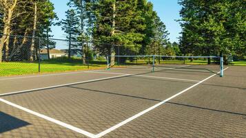 Cancha de tenis al aire libre con red, rodeada de árboles y una valla.
